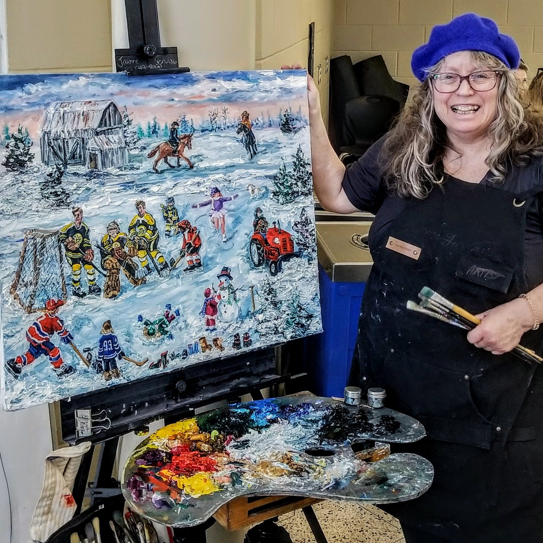 Joanne Gervais standing beside her painting of children playing hockey and ice skating. 